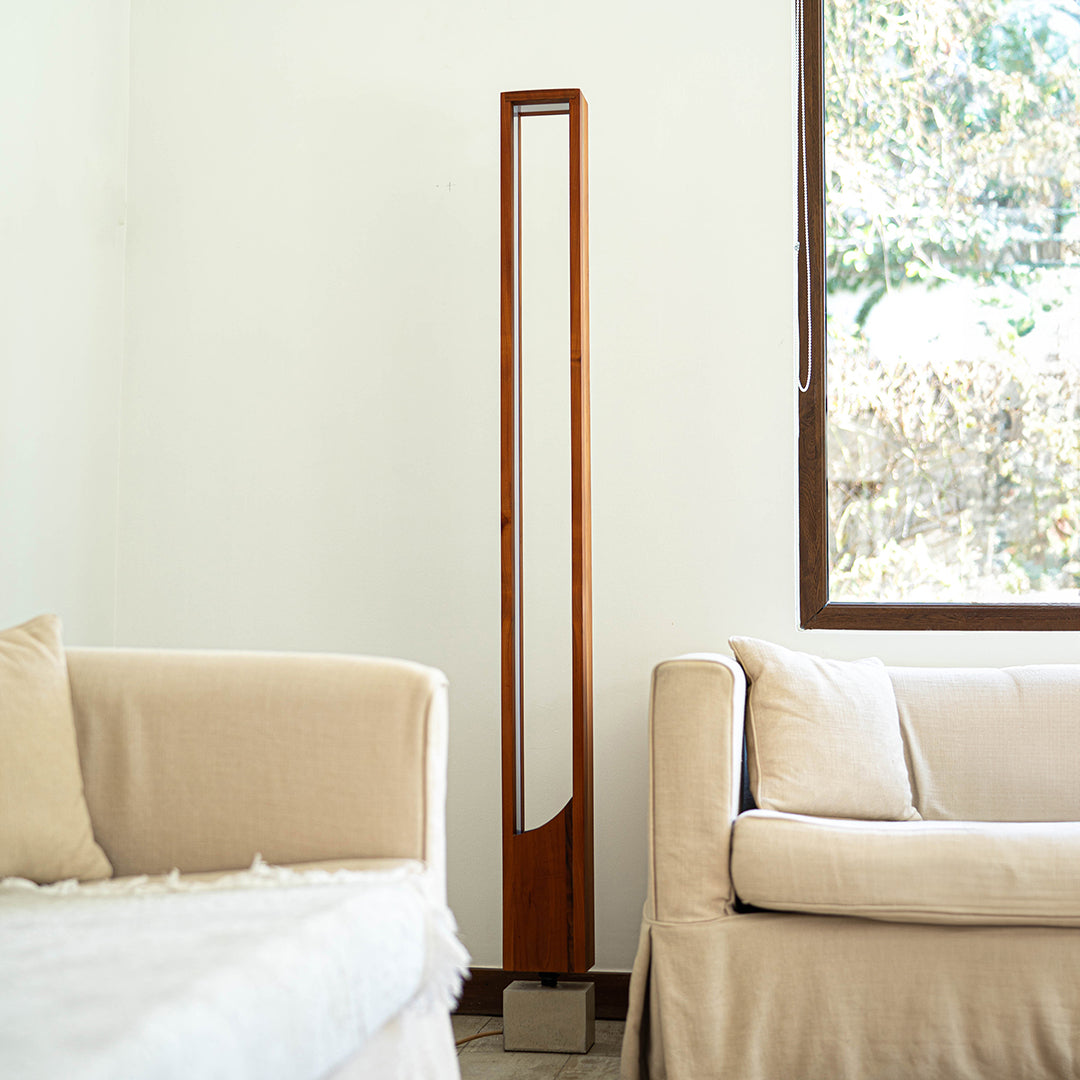  Lámpara de pie caliza en madera de raulí ubicada entre dos sillones con una ventana a su lado. Un perfecto uso para esta lámpara aportando un estilo moderno y natural a esta sala de estar.