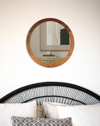 Espejo circular de una capa en madera de raulí colocado en la pared sobre una cama. Amplia tus espacios añadiendo al mismo tiempo un toque de naturaleza.