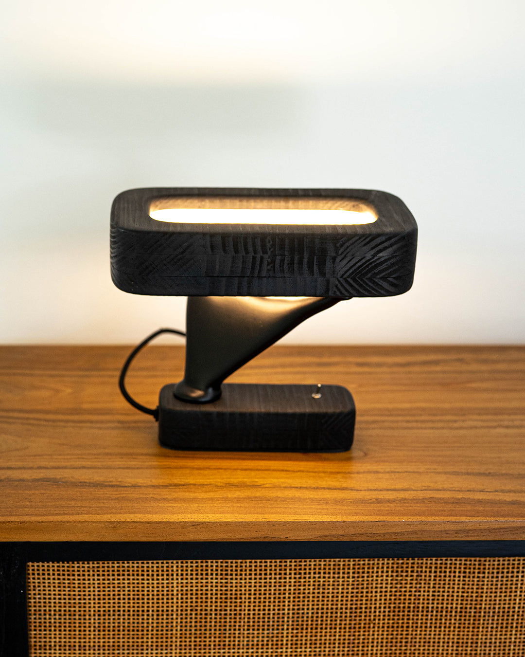 Lámpara de mesa de color negro en madera. Diseño contemporáneo y luz cálida encendida.